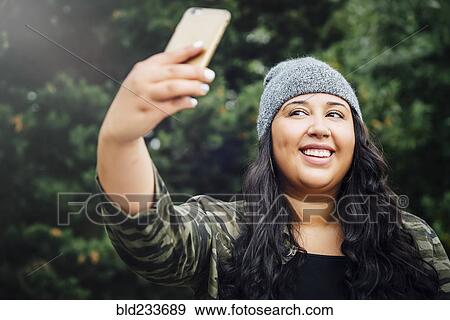 Mixed Race woman posing for cell phone selfie in forest View Large Photo Image Stock Photo - Mixed Race woman posing for cell phone selfie in forest. Fotosearch