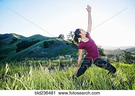 Stock Image - Mixed Race woman practicing yoga on hill. Fotosearch