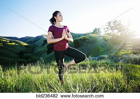 Stock Image - Mixed Race woman practicing yoga on hill. Fotosearch