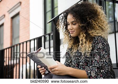 Stock Image - Mixed Race woman reading book in city. Fotosearch