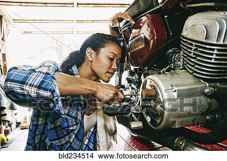 Mixed Race woman repairing motorcycle in garage View Large Photo Image Picture - Mixed Race woman repairing motorcycle in garage. Fotosearch