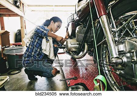 Stock Photography - Mixed Race woman repairing motorcycle in garage. Fotosearch