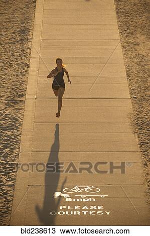 Stock Image - Mixed Race woman running on path near beach. Fotosearch