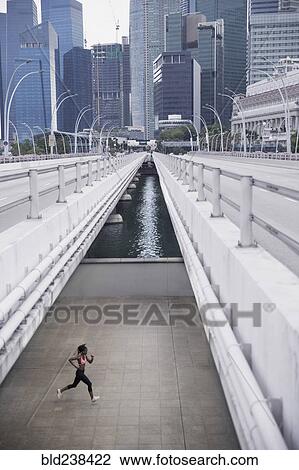 Stock Image - Mixed Race woman running under urban bridge. Fotosearch