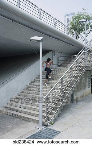Picture - Mixed Race woman running up urban staircase. Fotosearch