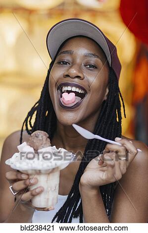 Stock Image - Mixed Race woman showing heart-shape candy on tongue. Fotosearch