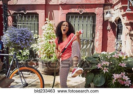 Stock Image - Mixed Race woman singing and playing air guitar in garden. Fotosearch