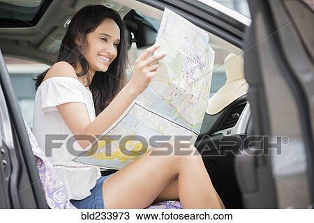 Stock Image - Mixed Race woman sitting in car reading map. Fotosearch