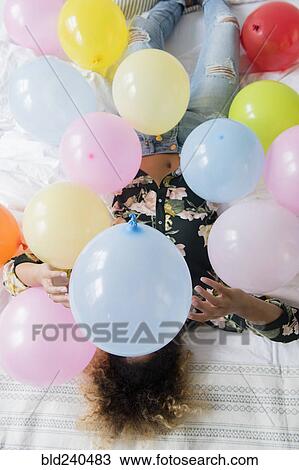 Mixed Race woman sitting on bed covered with balloons View Large Photo Image Stock Image - Mixed Race woman sitting on bed covered with balloons. Fotosearch