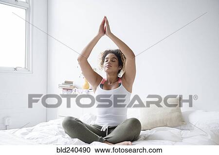 Mixed Race woman sitting on bed meditating View Large Photo Image Stock Image - Mixed Race woman sitting on bed meditating. Fotosearch