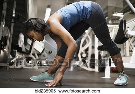 Stock Photography - Mixed Race woman stretching legs at gymnasium. Fotosearch