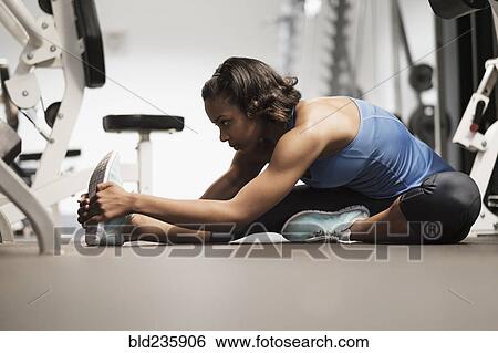 Stock Photograph - Mixed Race woman stretching legs on floor at gymnasium. Fotosearch