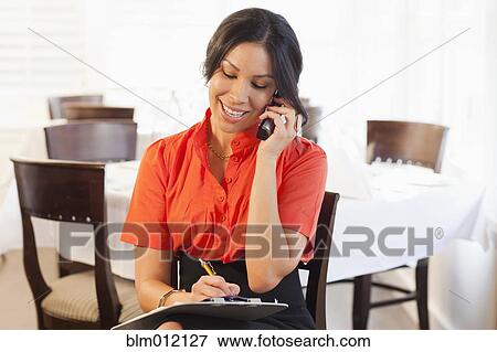 Stock Photo - Mixed race woman talking on telephone in restaurant. Fotosearch