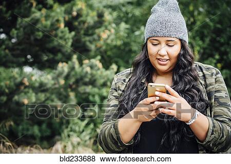 Mixed Race woman texting on cell phone in forest View Large Photo Image Stock Photo - Mixed Race woman texting on cell phone in forest. Fotosearch