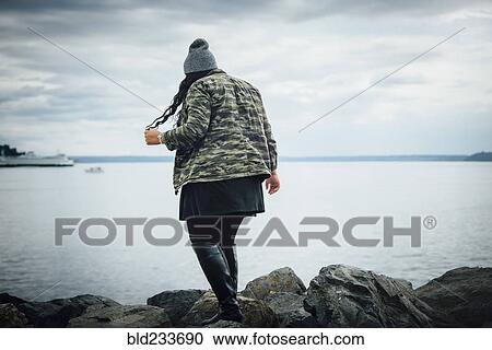 Stock Image - Mixed Race woman walking on rocks near ocean. Fotosearch