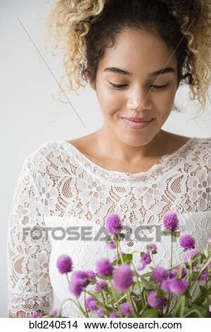 Picture - Mixed Race woman wearing wedding dress admiring bouquet. Fotosearch