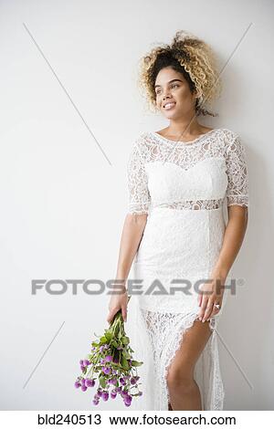 Stock Image - Mixed Race woman wearing wedding dress leaning on wall. Fotosearch