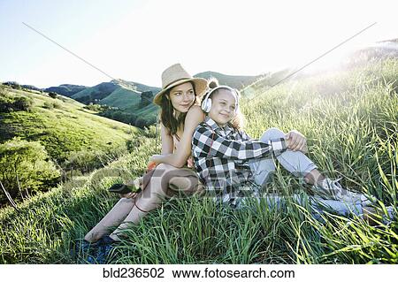 Stock Image - Mother and daughter sitting on hill listening to headphones. Fotosearch