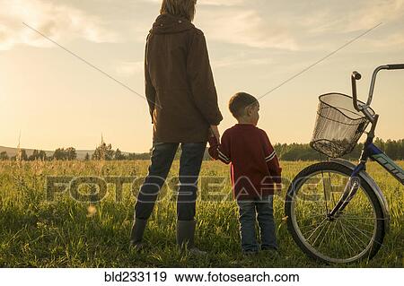 Stock Photo - Mother and son holding hands in field near bicycle. Fotosearch