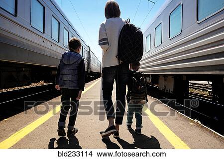 Picture - Mother and sons walking between trains at train station. Fotosearch