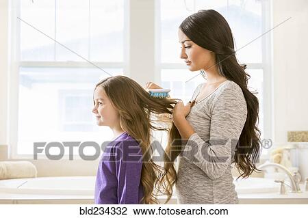 Stock Image - Mother brushing hair of daughter in bathroom. Fotosearch