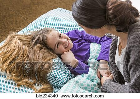 Stock Image - Mother comforting daughter at bedtime. Fotosearch