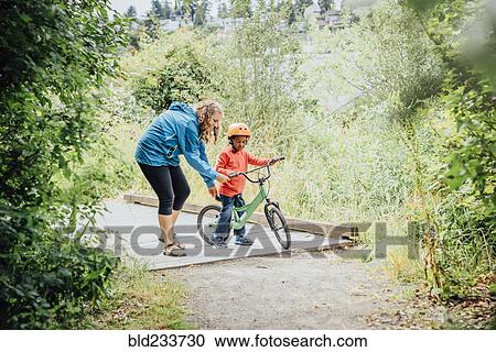 Mother helping son ride bicycle View Large Photo Image Stock Image - Mother helping son ride bicycle. Fotosearch