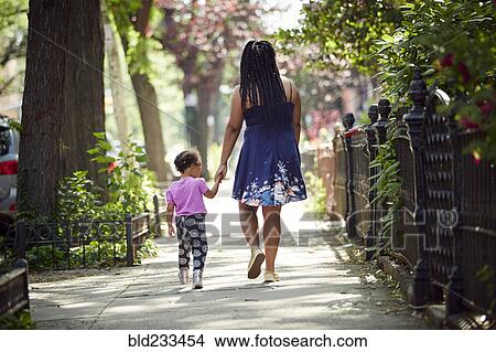 Picture - Mother walking daughter on city sidewalk. Fotosearch