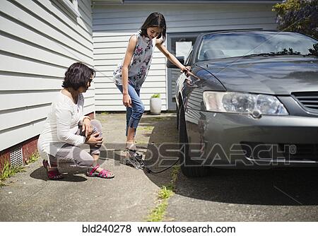 Stock Photo - Mother watching daughter inflating car tire. Fotosearch