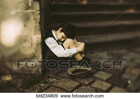 Stock Photo - Old-fashioned Caucasian boy sitting near staircase begging for money. Fotosearch