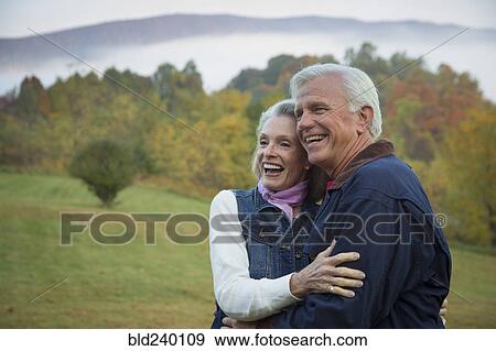 Stock Photo - Older Caucasian couple hugging in field. Fotosearch