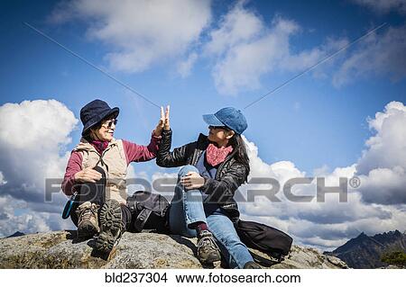 Picture - Older Japanese mother and daughter high-fiving on rock. Fotosearch