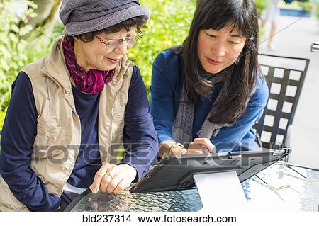 Picture - Older Japanese mother and daughter using digital tablet. Fotosearch