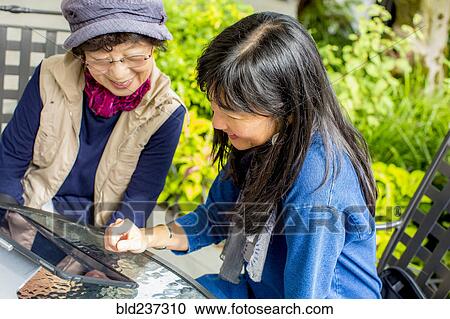 Stock Image - Older Japanese mother and daughter using digital tablet. Fotosearch
