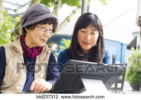 Stock Image - Older Japanese mother and daughter using digital tablet. Fotosearch