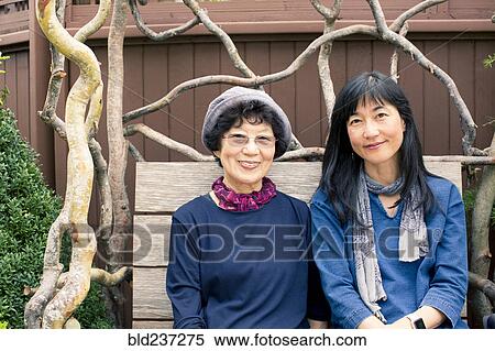 Stock Photography - Older Japanese mother and daughter sitting on wooden bench. Fotosearch