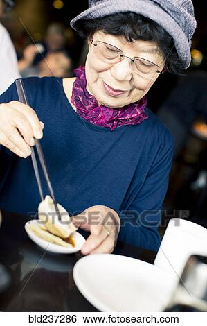 Stock Photograph - Older Japanese woman eating food with chopsticks. Fotosearch