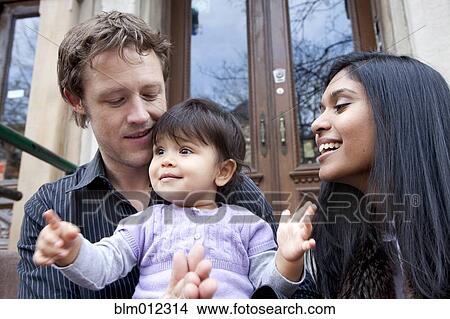 Picture - Parent's sitting on front stoop with baby girl. Fotosearch