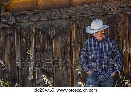 Stock Photo - Pensive Caucasian farmer leaning on wooden fence. Fotosearch