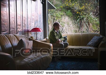 Pensive Caucasian man sitting on sofa near window View Large Photo Image Stock Photo - Pensive Caucasian man sitting on sofa near window. Fotosearch