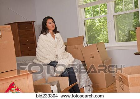 Picture - Pensive Hispanic woman sitting on bed near moving boxes. Fotosearch
