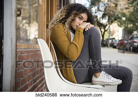 Stock Photo - Pensive Mixed Race woman sitting on chair in city. Fotosearch