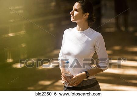 Pensive woman holding water bottle in sunny forest View Large Photo Image Stock Photograph - Pensive woman holding water bottle in sunny forest. Fotosearch