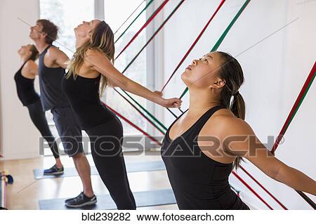 Stock Image - People pulling on resistance bands in gymnasium. Fotosearch