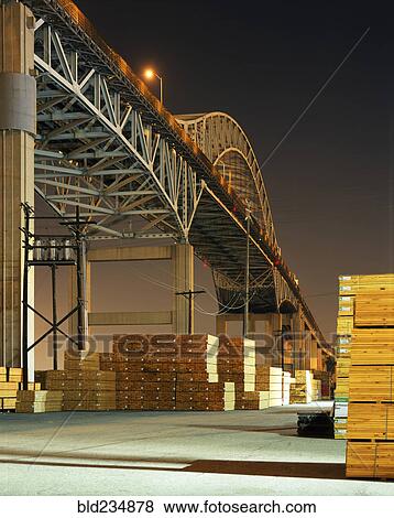 Stock Photo - Piles of lumber under bridge at night. Fotosearch