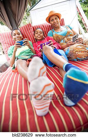 Stock Photo - Portrait of Black mother and twin sons using cell phones outdoors. Fotosearch