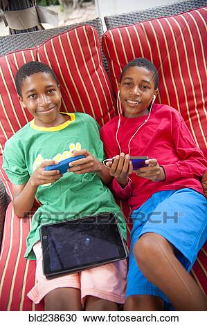 Stock Image - Portrait of Black twin boys using cell phones outdoors. Fotosearch