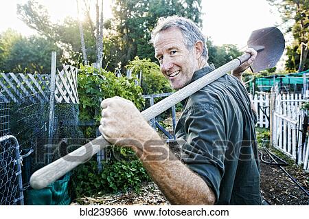 Stock Photograph - Portrait of Caucasian man carrying shovel in garden. Fotosearch