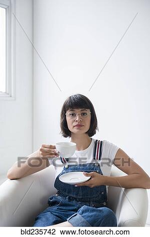 Stock Image - Portrait of Hispanic woman drinking coffee in armchair. Fotosearch