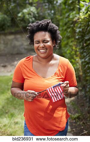 Stock Image - Portrait of laughing Black woman holding little American flag. Fotosearch